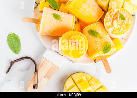 Eis, Eis am Stiel. Organische diätetische Lebensmittel, Desserts. Gefrorenes Mango Smoothie, mit Minze und frischen Mango Obst, auf Platte, auf weissem Marmortisch. Stockfoto