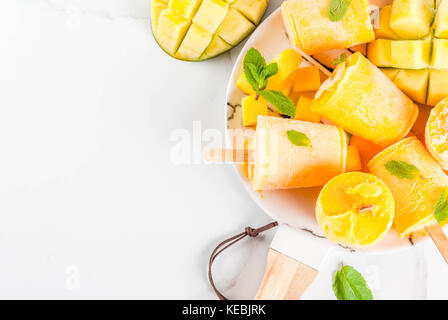Eis, Eis am Stiel. Organische diätetische Lebensmittel, Desserts. Gefrorenes Mango Smoothie, mit Minze und frischen Mango Obst, auf Platte, auf weissem Marmortisch. Stockfoto