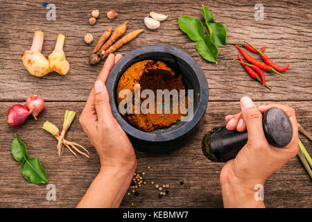 Die Frauen halten mit Mörser und Pistill spice Red Curry Paste Wirkstoff von Thai beliebte Speisen auf rustikalen Holzmöbeln Hintergrund. Gewürze Zutaten Chili, pe Stockfoto