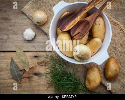 Frische organische Kartoffeln in Hanf willen Tasche mit Zutaten und Kräutern auf rustikalen Holztisch Vorbereitung für das Kochen. Stockfoto