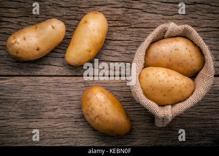 Frische organische Kartoffeln in Hanf willen Beutel auf rustikalen Holzmöbeln Hintergrund. Zeile bio Kartoffeln auf alten hölzernen Hintergrund mit kopieren. Stockfoto