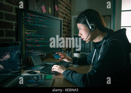 Schönheit attraktive hacker Frau mit Kopfhörer und Holding Kreditkarte tun Telekommunikation betrug. Stockfoto