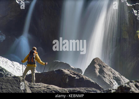 Wandern Mann mit Rucksack auf Wasserfall im schönen Sommer Natur Landschaft. Portrait von erwachsenen männlichen Rücken outdoor. Stockfoto