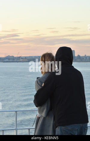 Ein paar Liebhaber kuscheln und romantisch Umarmen mit Blick auf das Meer bei Sonnenuntergang über dem Hafen in einer ruhigen Abend miteinander und liebevolle Umarmung. Stockfoto