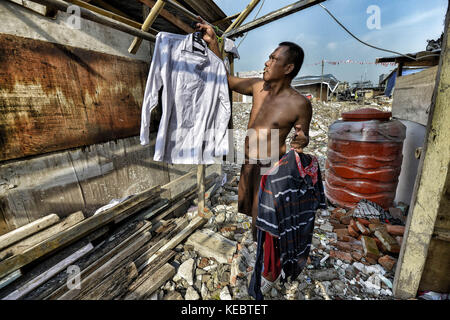 Jakarta, Java, Indonesien. August 2016. Ein Mann wird gesehen, wie er seine Kleidung in der Nachbarschaft von Pasar Ikan in Jakarta wäscht. Im April letzten Jahres stürmten Hunderte von Soldaten und Polizisten Pasar Ikan, ein historisches Fischerviertel nördlich von Jakarta, und machten alles in Trümmer. Wo es Backsteinhäuser gab, jetzt gibt es Berge von Schutt und Zelten. Die Einwohner zögern, die Nachbarschaft zu verlassen und weigern sich, in die von den Behörden gewährten Schutzhütten zu ziehen, weil sie behaupten, sie könnten sich diese nicht leisten. Es handelt sich um Räumungen ohne Ankündigung oder Gerichtsverfahren Stockfoto