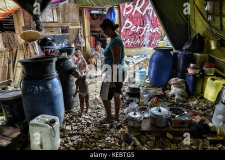 Jakarta, Java, Indonesien. August 2016. Eine Familie wird beim Kochen in einem der provisorischen Zelte im Pasar Ikan Viertel von Jakarta gesehen. Im April letzten Jahres stürmten Hunderte von Soldaten und Polizisten Pasar Ikan, ein historisches Fischerviertel nördlich von Jakarta, und machten alles in Trümmer. Wo es Backsteinhäuser gab, jetzt gibt es Berge von Schutt und Zelten. Die Einwohner zögern, die Nachbarschaft zu verlassen und weigern sich, in die von den Behörden gewährten Schutzhütten zu ziehen, weil sie behaupten, sie könnten sich diese nicht leisten. Es sind Vertreibungen mit einem Stockfoto