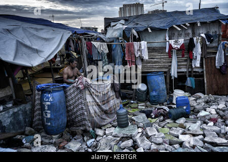 Jakarta, Java, Indonesien. August 2016. Ein Mann duscht auf der Straße mit dem Wasser aus den Trommeln in der Nachbarschaft Pasar Ikan in Jakarta. Im April letzten Jahres stürmten Hunderte von Soldaten und Polizisten Pasar Ikan, ein historisches Fischerviertel nördlich von Jakarta, und machten alles in Trümmer. Wo es Backsteinhäuser gab, jetzt gibt es Berge von Schutt und Zelten. Die Einwohner zögern, die Nachbarschaft zu verlassen und weigern sich, in die von den Behörden gewährten Schutzhütten zu ziehen, weil sie behaupten, sie könnten sich diese nicht leisten. Sie sind Evicti Stockfoto