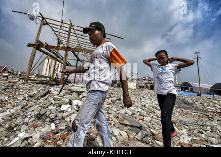 Jakarta, Java, Indonesien. August 2016. Ein Mann und seine Tochter gehen durch die Ruinen ihres alten Viertels Pasar Ikan in Jakarta. Im April letzten Jahres stürmten Hunderte von Soldaten und Polizisten Pasar Ikan, ein historisches Fischerviertel nördlich von Jakarta, und machten alles in Trümmer. Wo es Backsteinhäuser gab, jetzt gibt es Berge von Schutt und Zelten. Die Einwohner zögern, die Nachbarschaft zu verlassen und weigern sich, in die von den Behörden gewährten Schutzhütten zu ziehen, weil sie behaupten, sie könnten sich diese nicht leisten. Das sind Vertreibungen mit fast Stockfoto