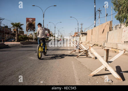 Kirkuk, Kirkuk, Irak. Oktober 2017. Ein Junge radelt durch das fast verlassene kurdische Viertel Kirkuk, vorbei an einem Plakat von Barzani, das während des Konflikts in den letzten 48 Stunden verbrannt wurde. Quelle: Elizabeth Fitt/SOPA/ZUMA Wire/Alamy Live News Stockfoto