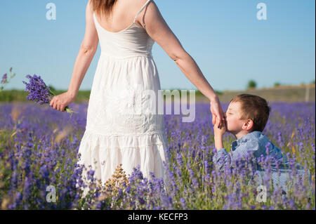 Süßes kleines Kind küssen Hand seiner Mutter mit Liebe und Zärtlichkeit unter blühenden Lavendel Feld Stockfoto