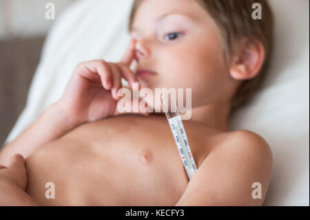 Lag und hatte wenig kaukasischen Jungen mit Thermometer in der Achselhöhle Stockfoto