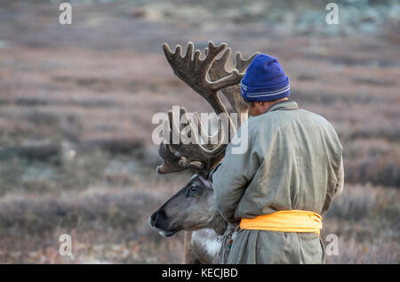 Tsaatan Mann, in einem traditionellen Deel gekleidet, mit seinen Rentieren in der Taiga im Norden der Mongolei Stockfoto