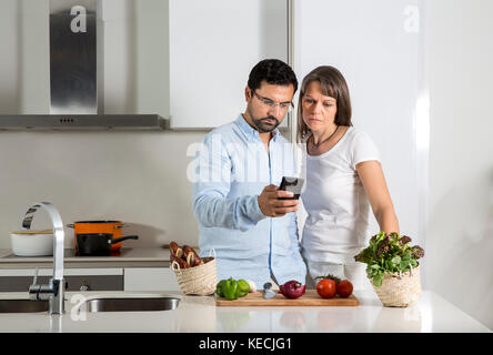 Paar an ein Mobiltelefon in einer Küche suchen Stockfoto