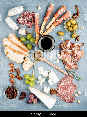 Fleisch und Käse Vorspeise Auswahl oder Wein Snack. Auswahl an Käse, Salami, Schinken, Brot, Baguette, Honig, Trauben, Oliven, getrocknete Tomaten, Pekannuss über grauer Beton texturierter Hintergrund, Ansicht von oben. Stockfoto