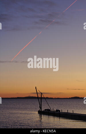 Pier vor Sonnenaufgang mit kleinen Kran gegen den Morgen Himmel und leuchtend roten Kondensstreifen silhouetted Overhead Stockfoto