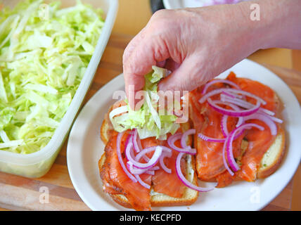 Ein Mann legt geschreddert Salat auf einen geräucherten Lachs Sandwich Stockfoto