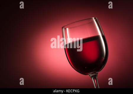 Rotwein in einem Weinglas auf rotem Hintergrund, Weinprobe, Luxus und Feier Konzept Stockfoto