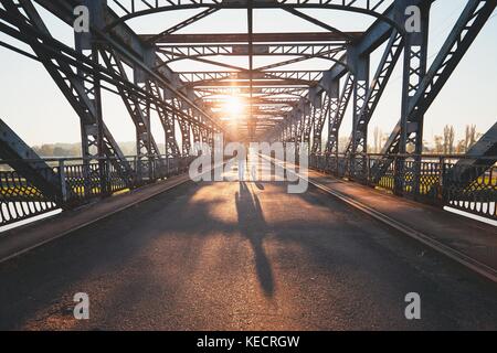 Morgen Spaziergang über den Fluss. Silhouetten und Schatten der Mann mit Hund auf der Iron Bridge. Stockfoto