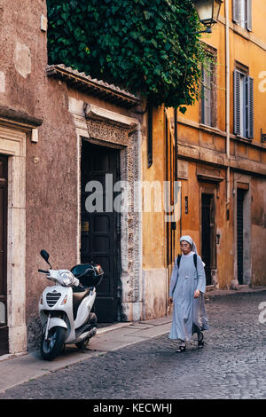 Eine Nonne geht der sonnenbeschienenen Straße in Richtung eines geparkten Roller in Rom, Italien, wo katholische Nonnen sind ein alltäglicher Anblick durch die Stadt Stockfoto