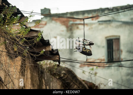 Alte Schuhe geworfen auf einem Draht (shoefitti) in einem alten Gebäude verschlissen oder Ruine Stockfoto