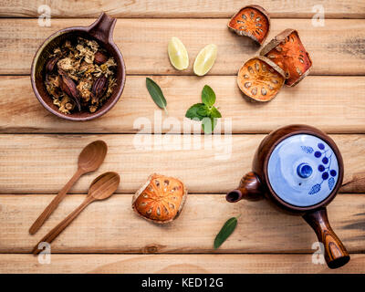 Kräutertee Topf mit frischen Kräutern Salbei, Pfefferminze, getrocknete indischen bael, getrocknete Chrysanthemen und Kalk Slice auf rustikalen Holzmöbeln Hintergrund. Stockfoto