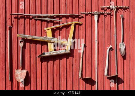 Bauernhof, alte Geräte hängen an einer roten Wand. Landwirtschaft Hintergrund Stockfoto