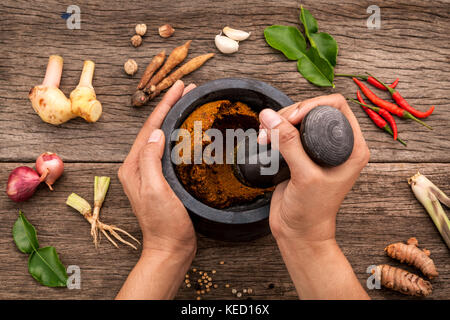 Die Frauen halten mit Mörser und Pistill spice Red Curry Paste Wirkstoff von Thai beliebte Speisen auf rustikalen Holzmöbeln Hintergrund. Gewürze Zutaten Chili, pe Stockfoto