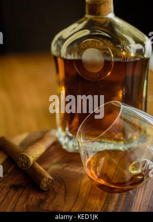 Nahaufnahme der beiden Zigarren, ein Glas und eine Flasche Rum auf einer hölzernen Oberfläche Stockfoto