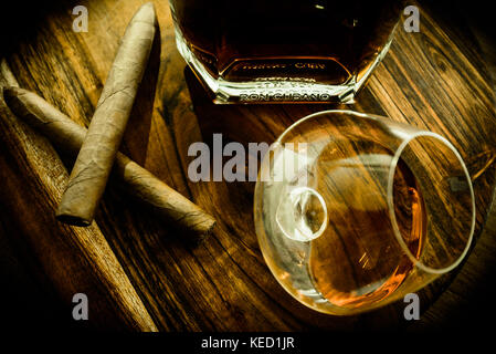 Blick von oben auf die zwei Zigarren, ein Glas und eine Flasche Rum auf einer hölzernen Oberfläche Stockfoto