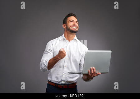 Ein glücklichen hübscher junger Mann hält einen Laptop und feiern Stockfoto