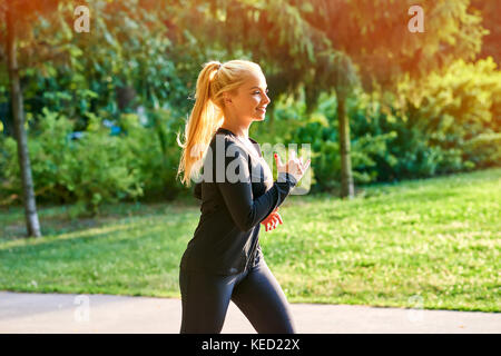 Eine schöne, junge blonde Frau mit schwarzen Kleidung, während in einem Park im Sonnenuntergang laufen Stockfoto