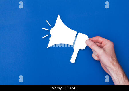 Männliche hand mit einem Lautsprecher Symbol vor einem blauen Hintergrund Stockfoto
