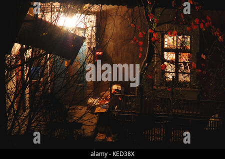 Altes Haus mit saturnische Rote Wände, eine Veranda erleuchtet von Lampe und Innenhof auf Herbstabend. Konzept der Herbst in einer kleinen Stadt. Ansicht von oben. Stockfoto