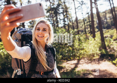 Frau machen Fotos mit dem Handy während des Trekking. Frau Wanderer klicken selfie während Trekking in einem Wald. Stockfoto