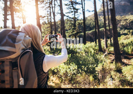 Frau machen Fotos mit dem Handy während des Trekking. Wanderer mit Rucksack fotografieren Wald Szenen. Stockfoto