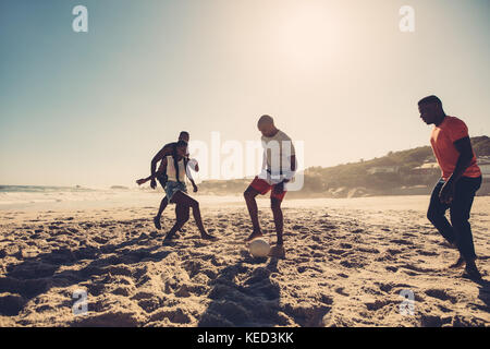 Gruppe von Freunden Spaß am Strand Fußball spielen. Junge Menschen Fußball spielen auf Sandstrand. Stockfoto