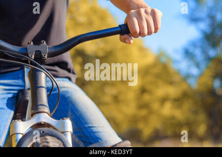 Nahaufnahme eines Menschen Hand in Jeans und einem schwarzen T-Shirt auf dem Lenkrad in einem off-road Fahrrad. Spaziergang an der frischen Luft im Herbst. Stockfoto