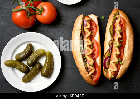 Hausgemachte heiße Hunde mit Tomaten, Gurken, Zwiebel mariniert auf dunklem Stein Hintergrund. top View Stockfoto