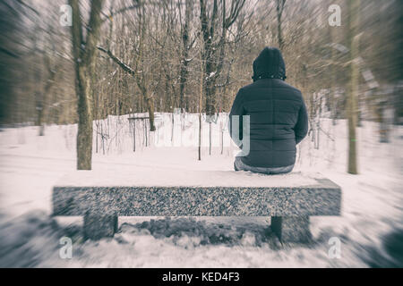 Mann sitzt auf der Bank in einem Wald im Winter mit Schnee auf dem Boden Stockfoto