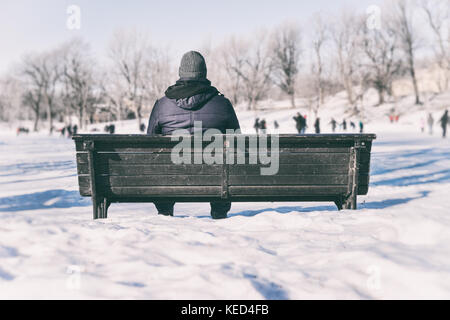 Mann sitzt auf der Bank mit Blick auf Leute Eislaufen Stockfoto