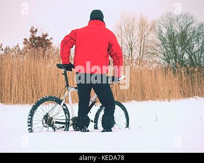 Sportler mit Mountainbike im Schnee verloren. verloren weg in tiefe Schneeverwehungen. Schneeflocken schmelzen in dunklen off road Reifen. Winter in das Feld ein. Stockfoto