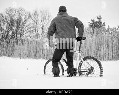 Sportler mit Mountainbike im Schnee verloren. verloren weg in tiefe Schneeverwehungen. Schneeflocken schmelzen in dunklen off road Reifen. Winter in das Feld ein. Stockfoto