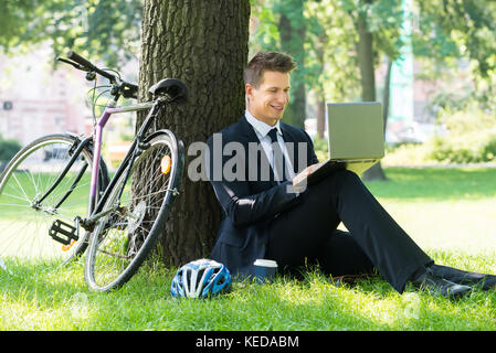 Lächelnden jungen männlichen Geschäftsmann mit Laptop im Park Stockfoto