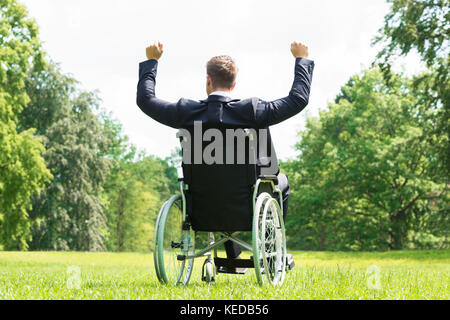 Ansicht der Rückseite des jungen Behinderten Mann im Rollstuhl mit Arm in Park angehoben Stockfoto