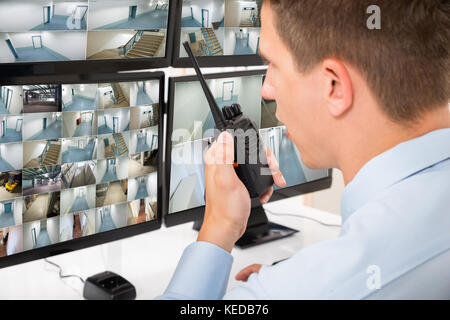 Nahaufnahme der männlichen Wachmann Mit walkie-talkie Während Überwachung mehrerer CCTV-Aufnahmen Stockfoto