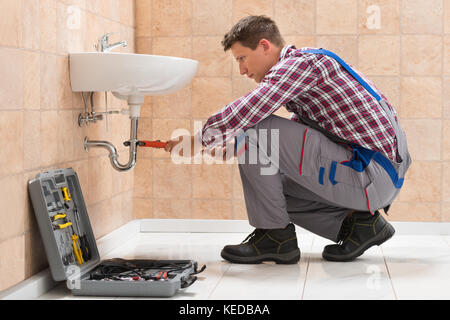 Junge männliche Klempner Armatur Spüle mit Schraubenschlüssel in Bad Stockfoto