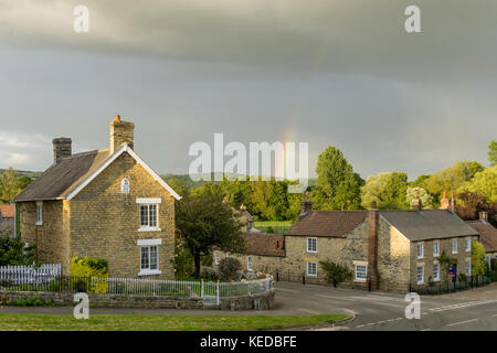 Der Kreuzung in der hübschen North Yorkshire Dorf Coxwold, mit einem Regenbogen über dem fernen Hügel Stockfoto