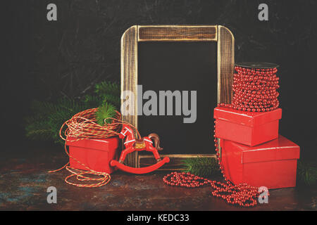 Schiefertafel und Weihnachtsschmuck und rote Geschenke Boxen auf dunklem Hintergrund Stockfoto