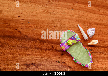 Lila baby Sandale mit Muscheln auf einer Holzmaserung Hintergrund angeordnet. minimalistischen Stil aussehen Stockfoto