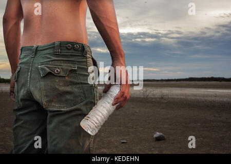 Mann hält eine Flasche Wasser Land auf den Boden trocknen Risse Stockfoto